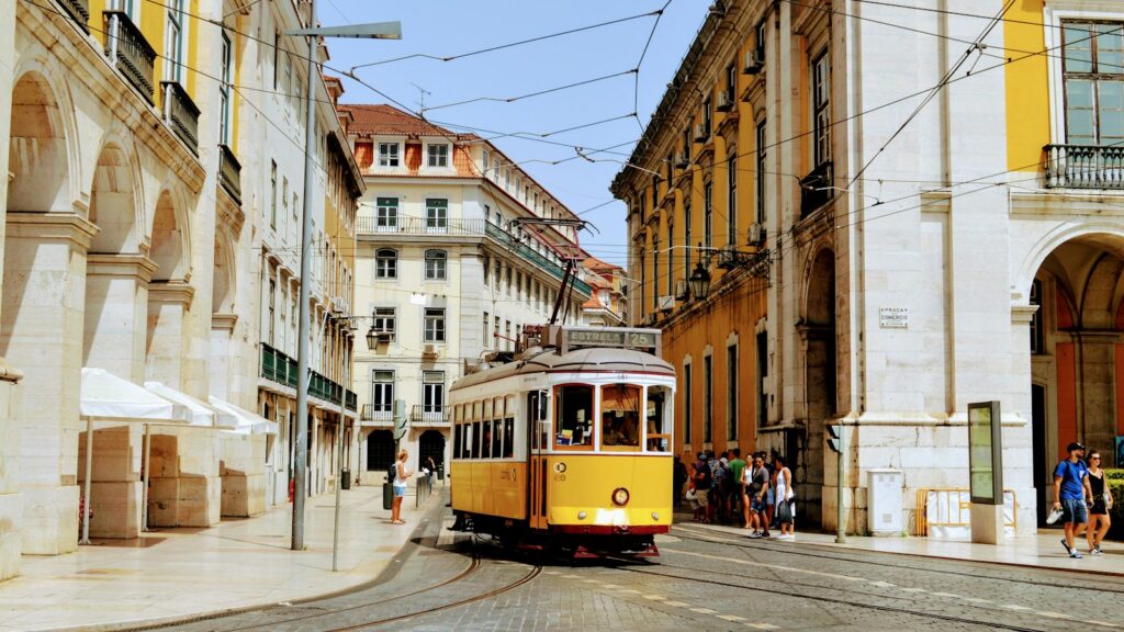 A yellow tram travelling through a historic street in Lisbon, Portugal